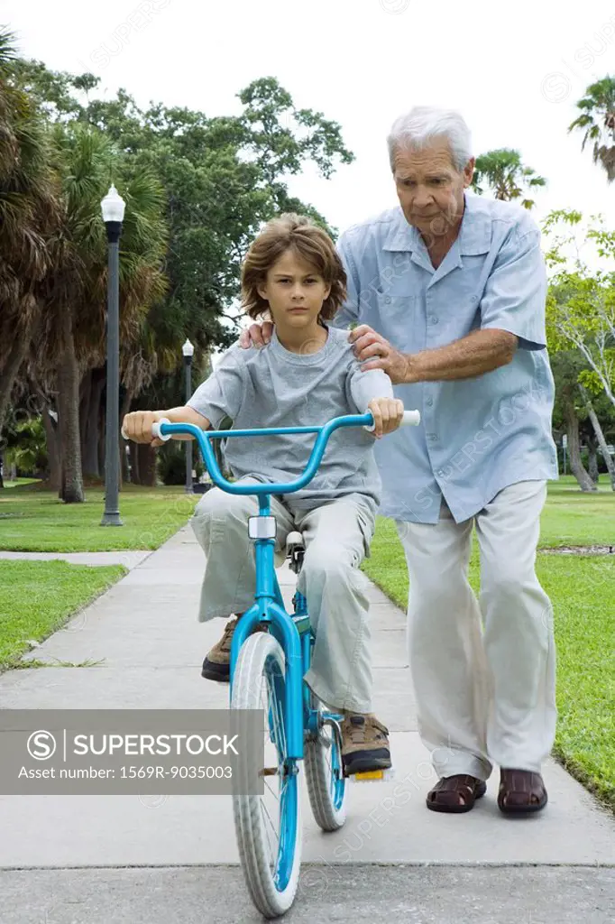 Grandfather teaching boy to ride bicycle, full length
