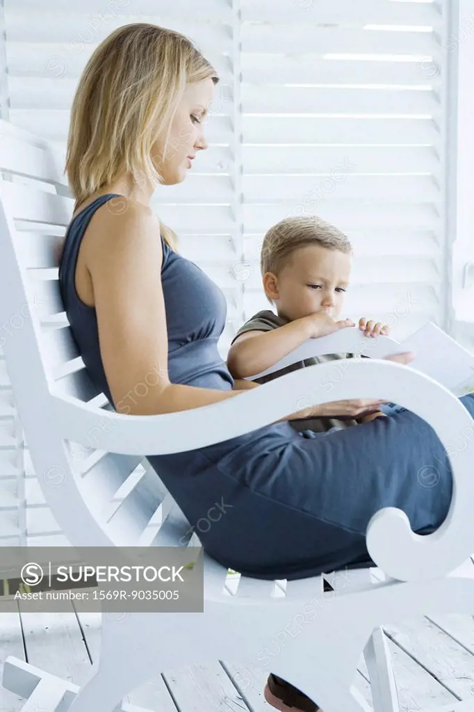 Woman sitting in rocking chair, looking at book with young son