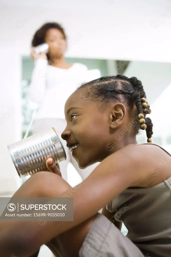 Girl speaking into tin can phone, mother listening in background