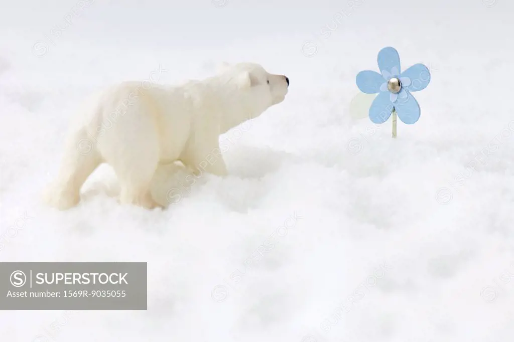 Toy polar bear in snow, looking at artificial flower
