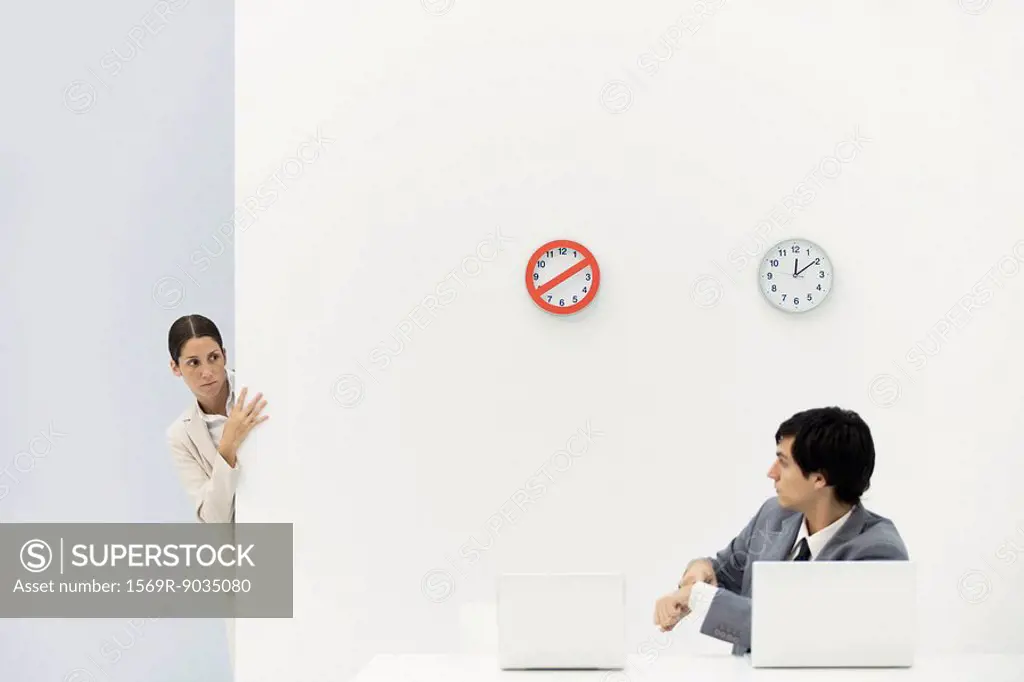 Woman peeking around corner as boss points at wristwatch, clocks on wall in background