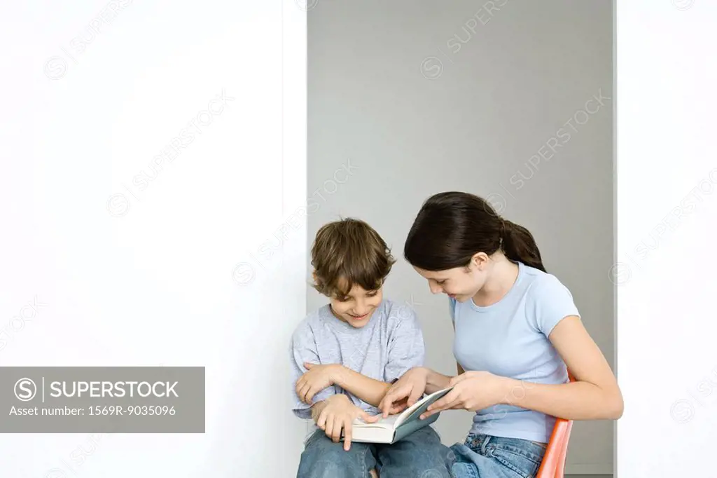 Preteen girl and little brother reading book together