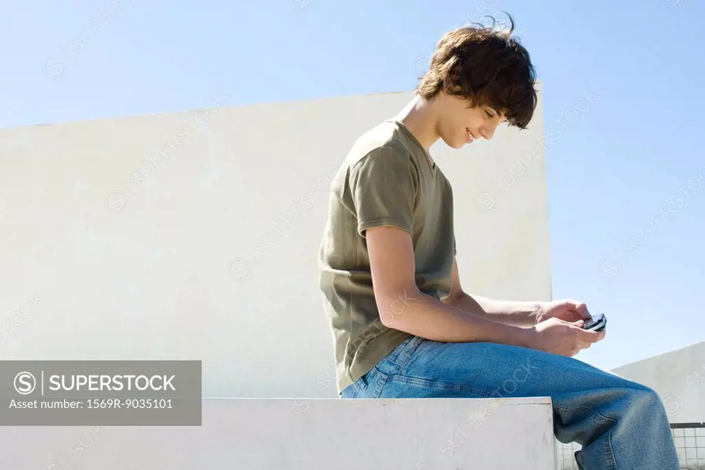 Teen boy playing handheld video game outdoors