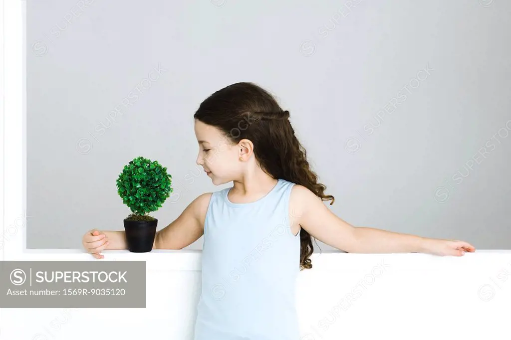 Little girl standing with arm around potted plant