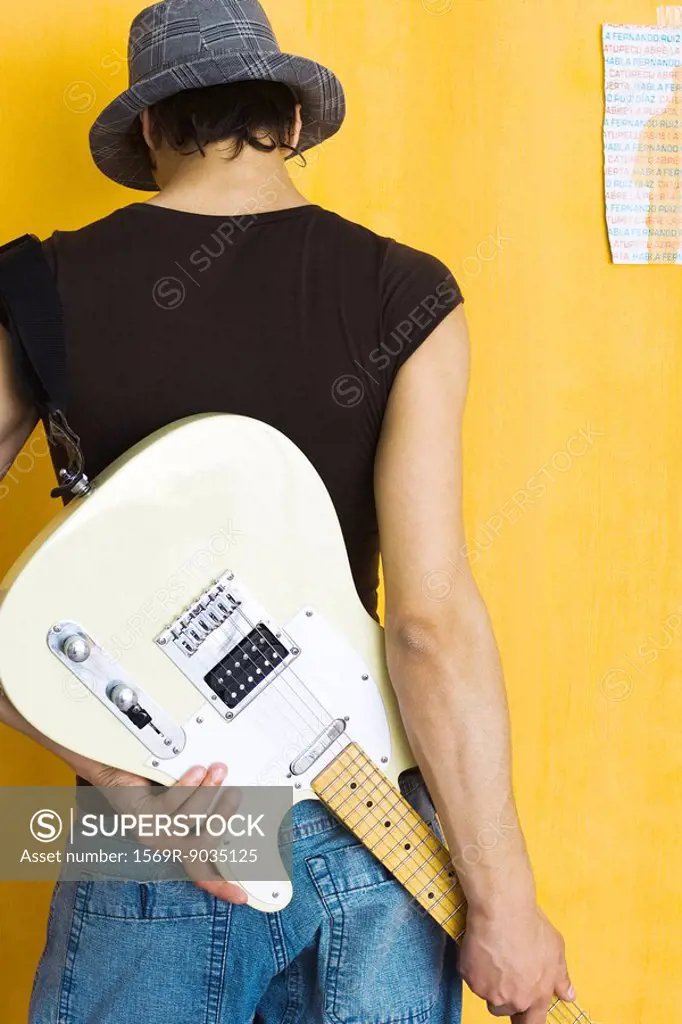 Young man holding electric guitar behind back, rear view