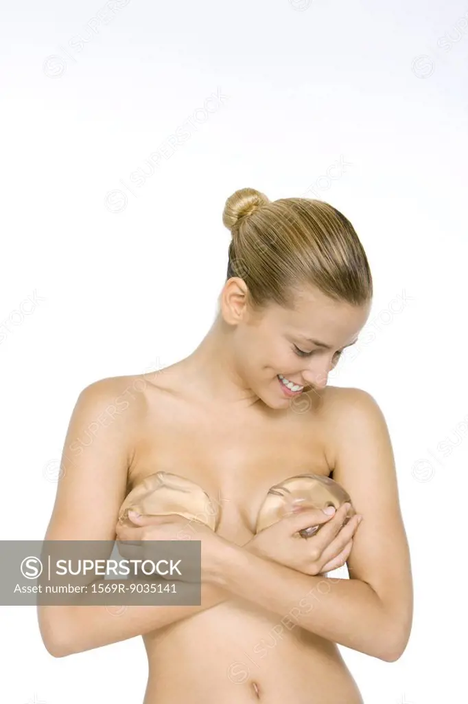 Woman holding silicone implants over breasts, looking down, smiling