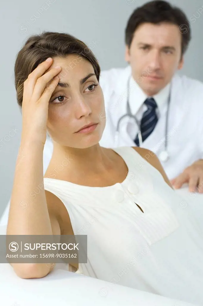 Woman holding head, looking away, doctor in background
