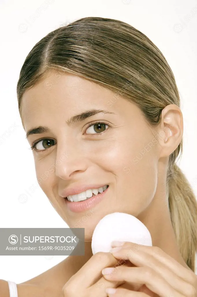 Woman using powder puff on cheek, smiling at camera
