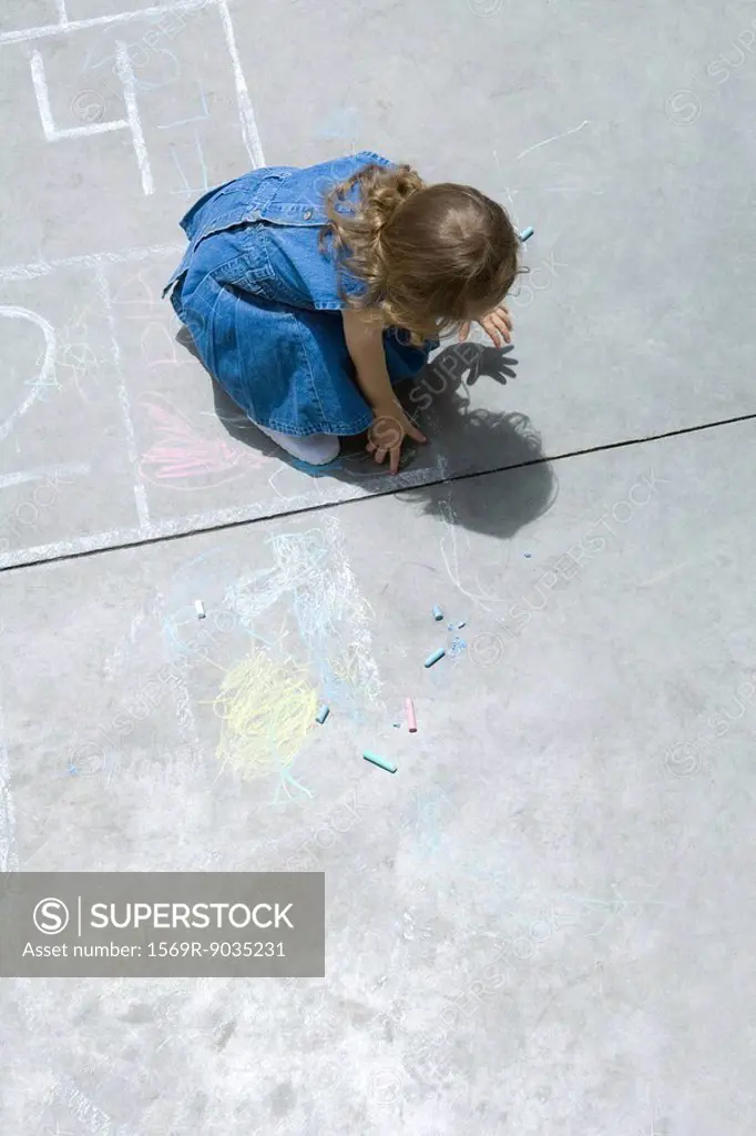 Girl playing with chalk, hunched over, high angle view