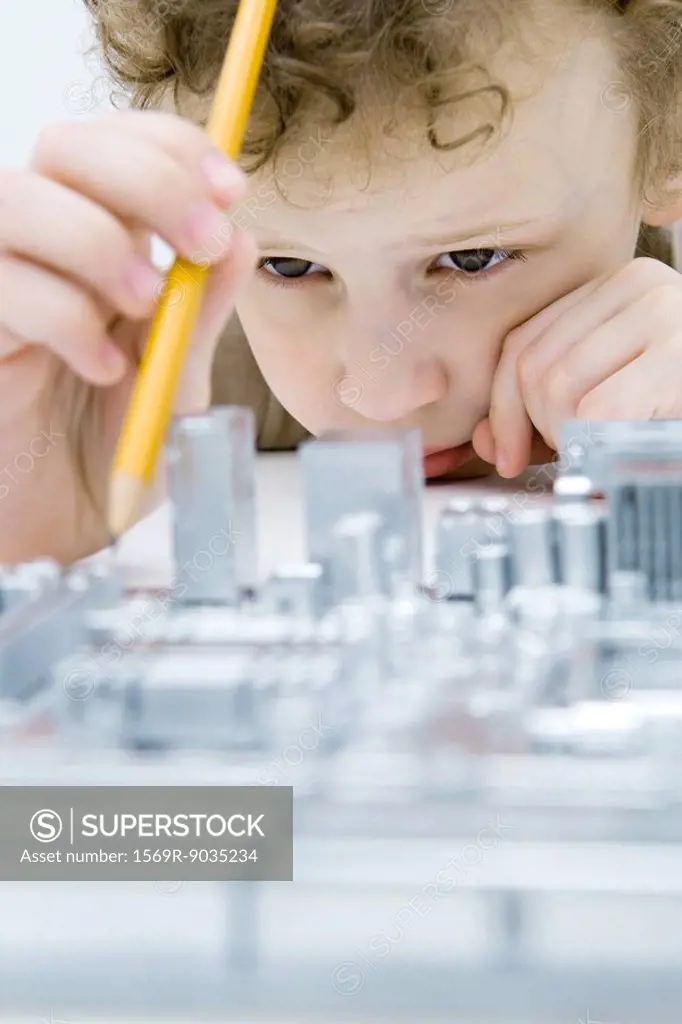 Little boy looking at circuit board, holding pencil, close-up
