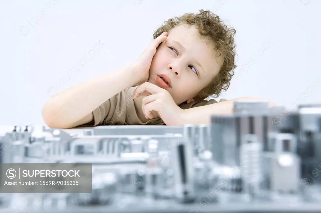 Little boy next to circuit board, holding head, looking up