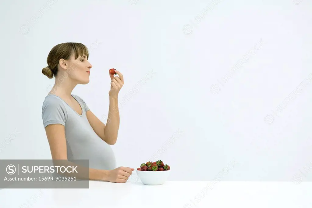 Pregnant woman eating strawberries from a bowl, side view
