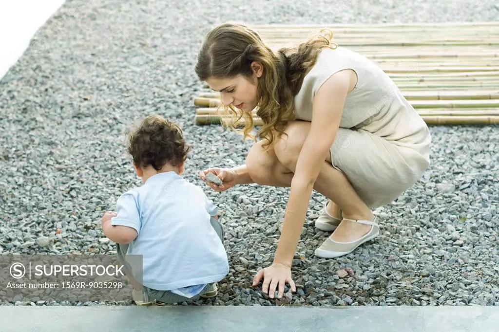 Mother and toddler crouching on gravel, looking at rocks