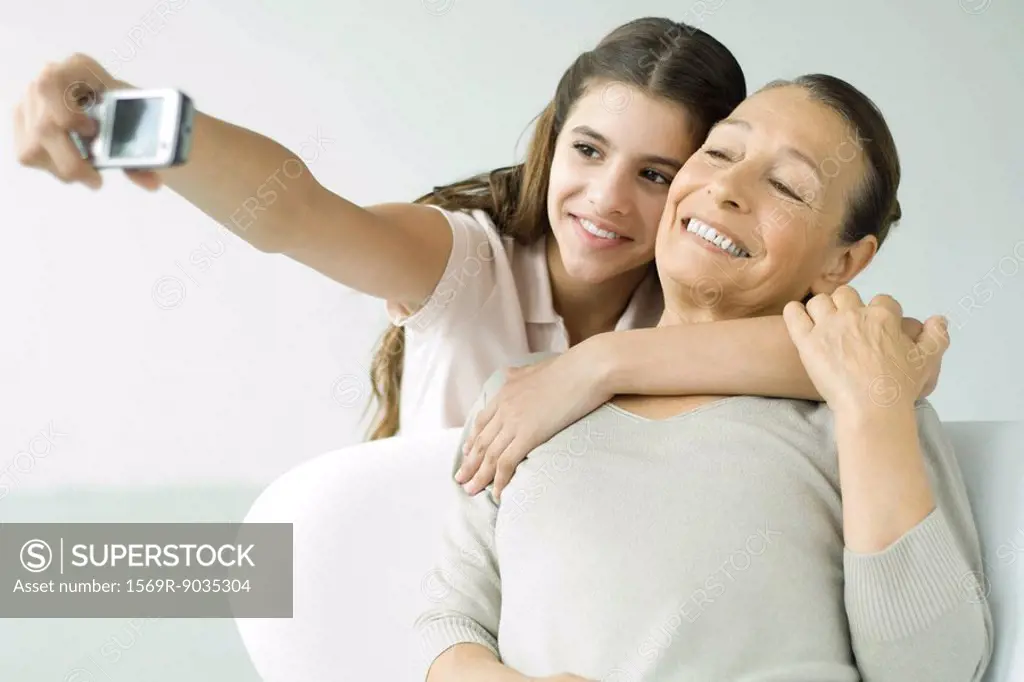 Preteen girl photographing self and grandmother with photophone, both smiling