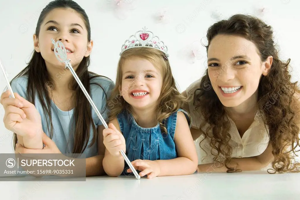 Mother and two daughters, smiling at camera, younger girl wearing tiara and holding wand