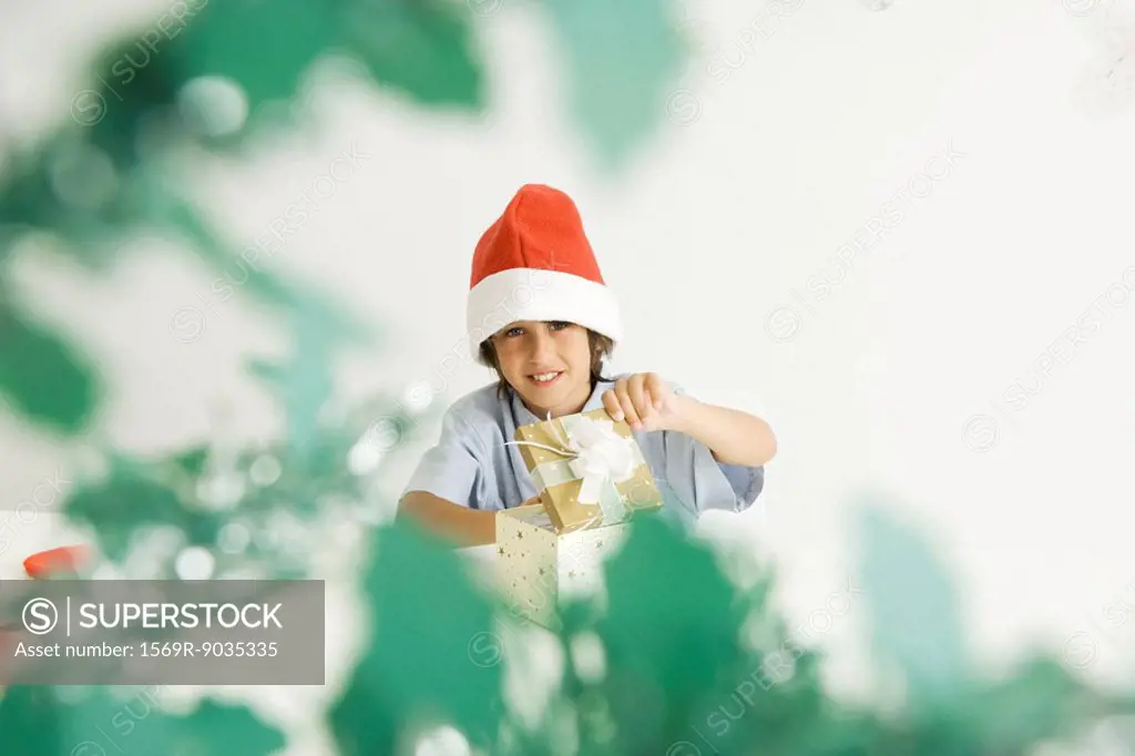 Boy opening Christmas gift, wearing Santa hat, smiling at camera