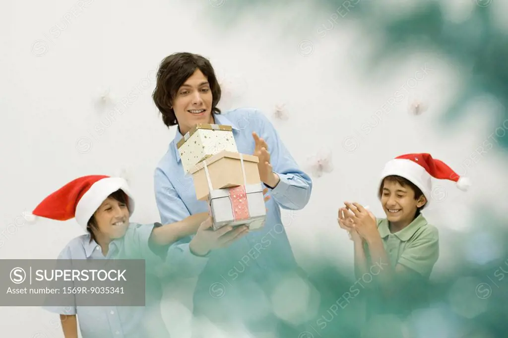 Boy knocking over stack of Christmas gifts in his older brother´s arms, smiling