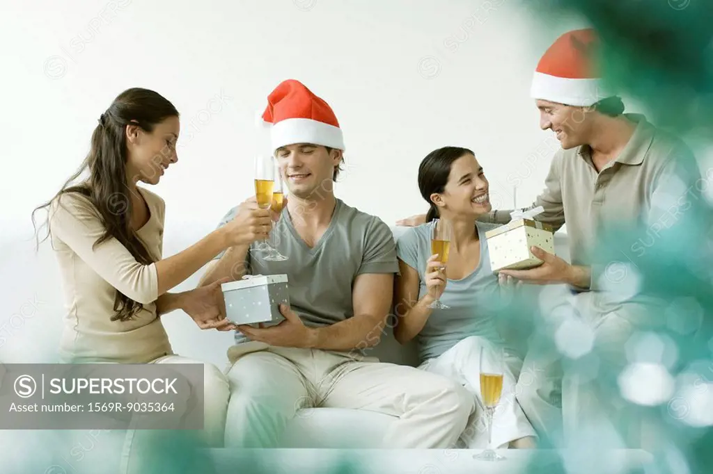 Two couples exchanging Christmas gifts, drinking champagne, men wearing Santa hats