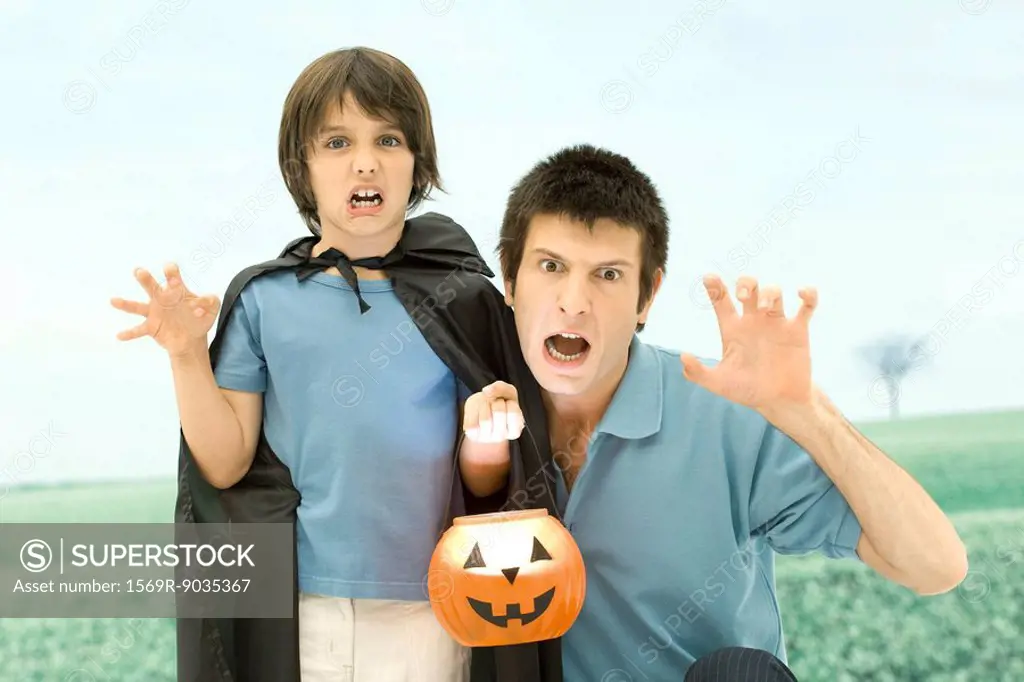Father and son holding jack o´lantern, making scary faces at camera