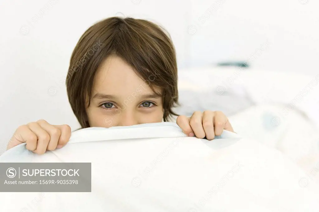 Little boy pulling sheet over his face, looking at camera