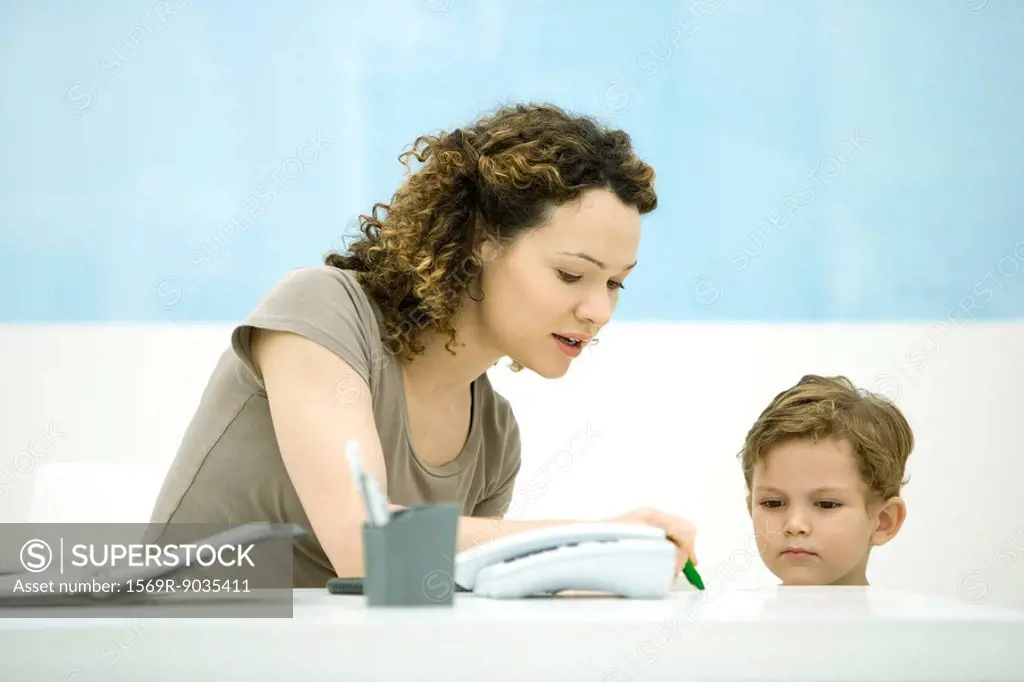 Young mother sitting at desk, interacting with little boy