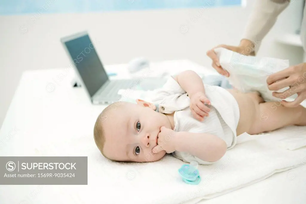 Mother changing baby´s diaper on desk, laptop in background