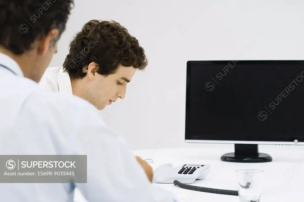 Businessmen sitting near phone and monitor