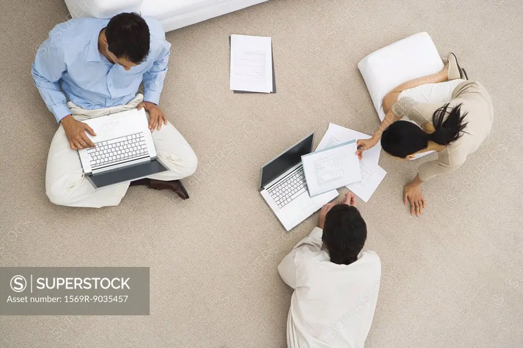Business associates sitting together on floor, using laptop computers, overhead view