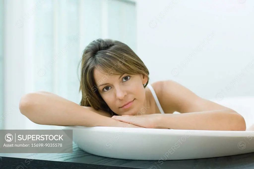 Woman in bathtub, head resting on arms, smiling at camera