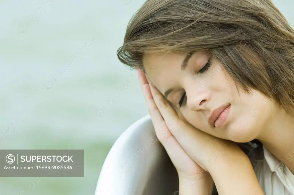 Teenage girl resting head on clasped hands, eyes closed, close-up