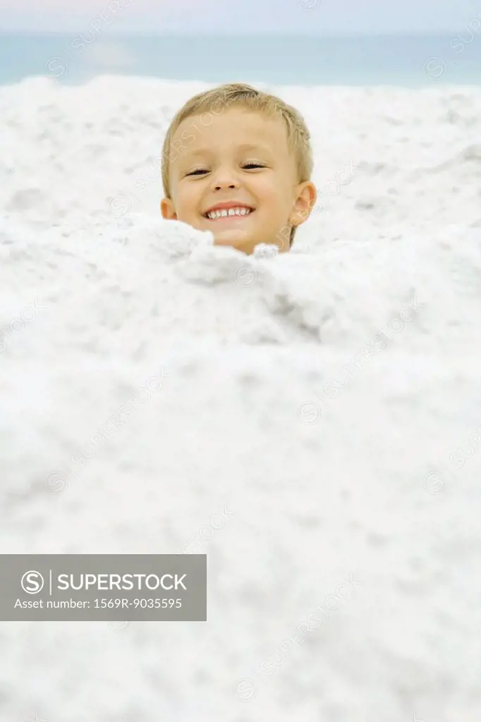 Boy´s head emerging from sand, smiling at camera