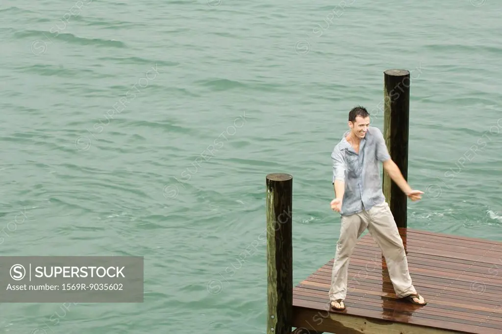 Man dancing on dock, getting wet, arms out, high angle view