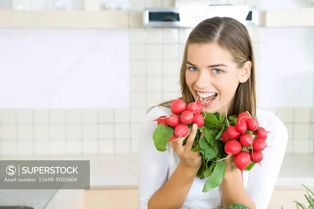 Woman holding up bunches of fresh radishes, smiling at camera