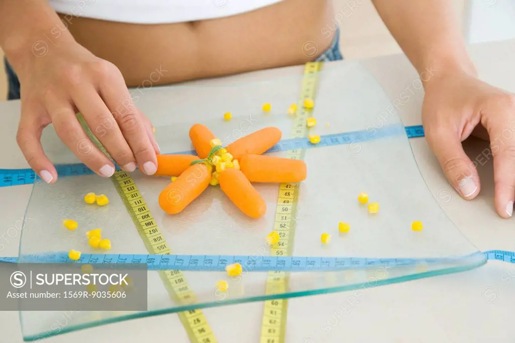 Woman arranging raw vegetables and measuring tapes, cropped view