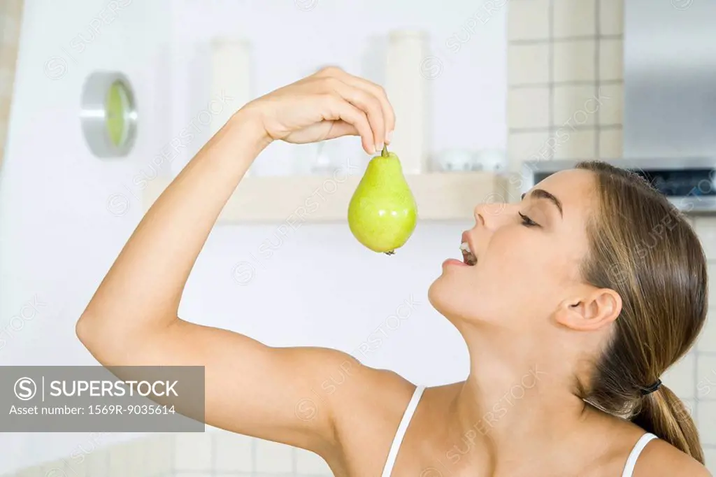 Woman holding up pear, head back, mouth open, side view