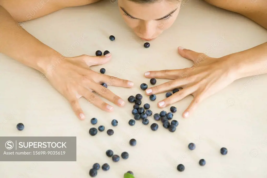 Woman leaning over scattered blueberries, cropped view