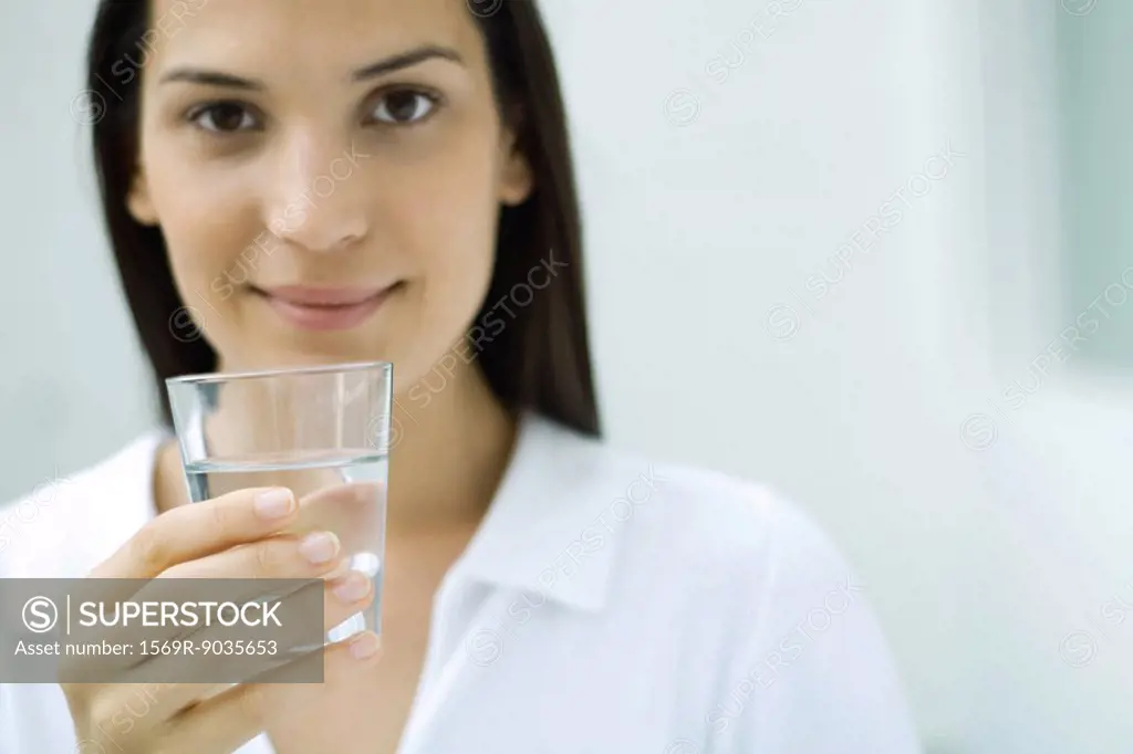 Woman holding glass of water, smiling at camera