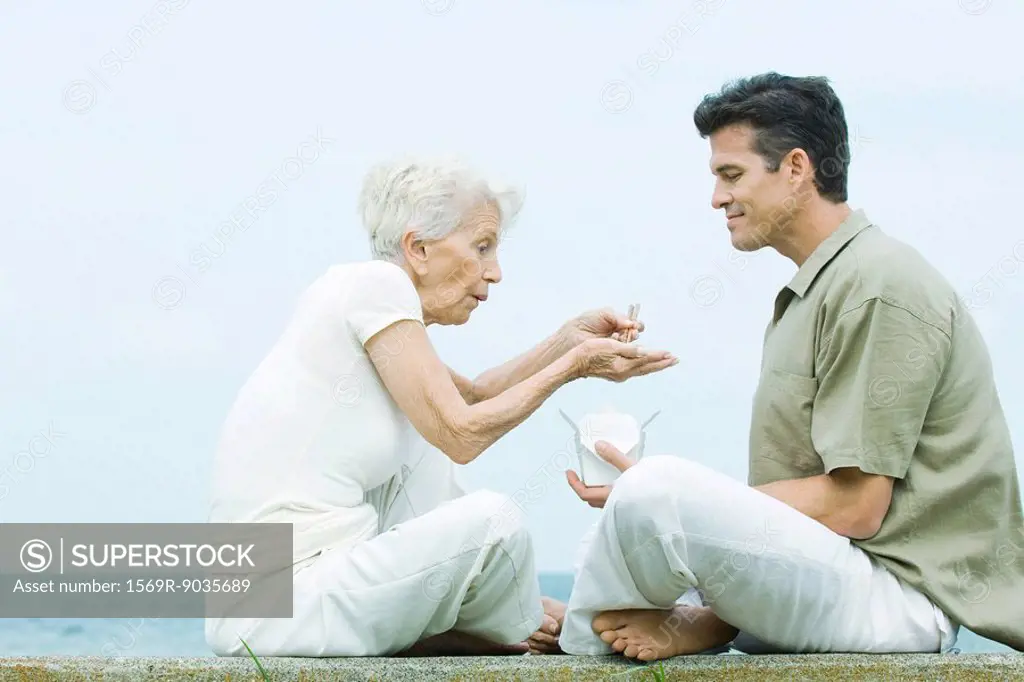 Senior woman and adult son sitting face to face, sharing take out food, side view