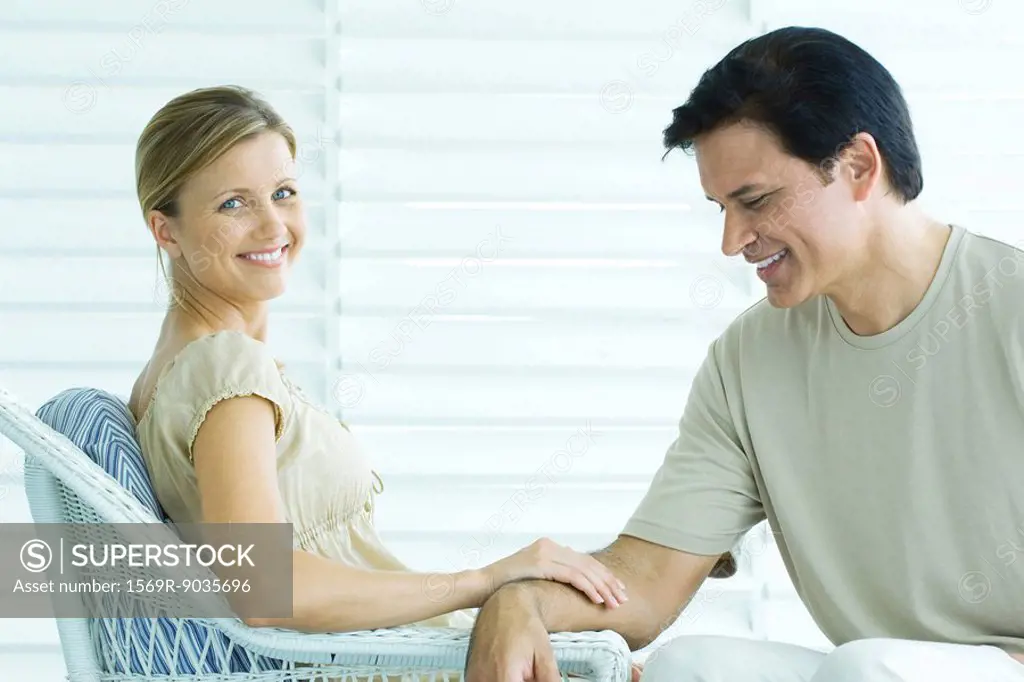 Couple sitting on porch, woman touching man´s arm and smiling at camera, man looking down