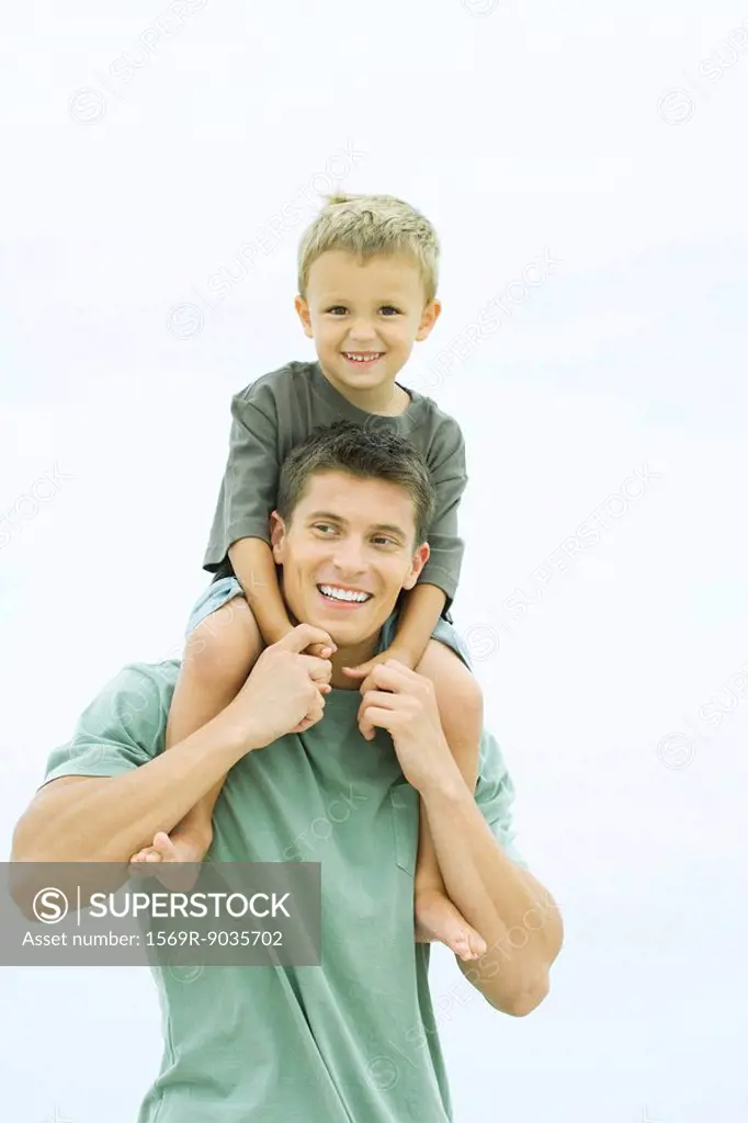 Father carrying son on shoulders, boy looking at camera, both smiling