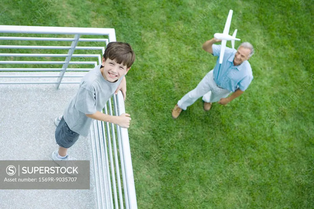 Grandson standing on balcony, grandfather standing below, holding toy airplane, high angle view