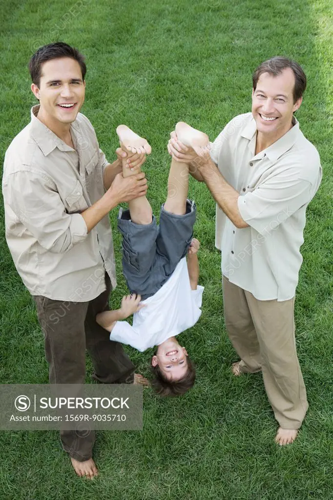 Two men holding little boy upside down by his legs, all smiling, high angle view