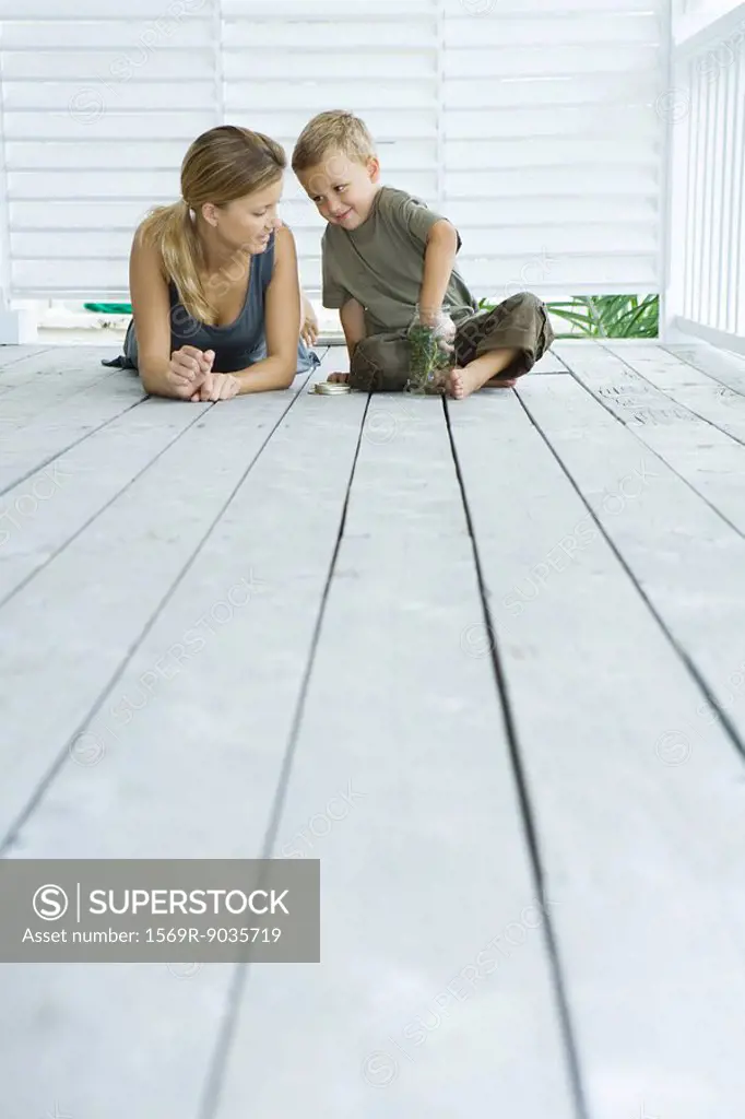 Mother and son on porch together, smiling at each other, boy with hand in jar, low angle view