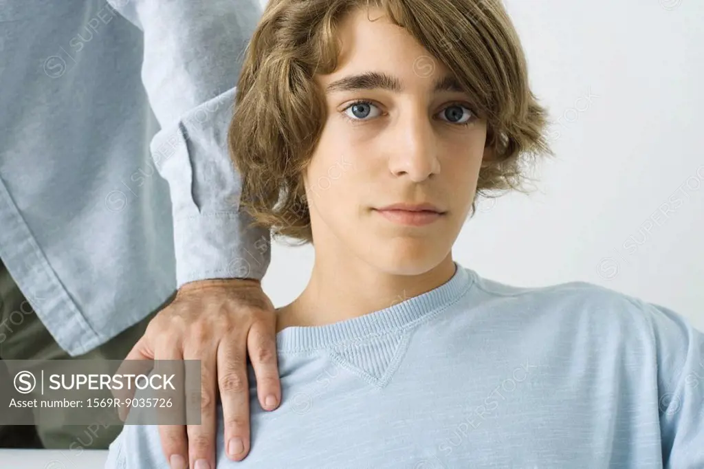 Teen boy with man´s hand on his shoulder, looking at camera