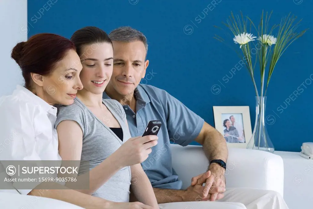 Teen girl on sofa with parents, looking at cell phone together