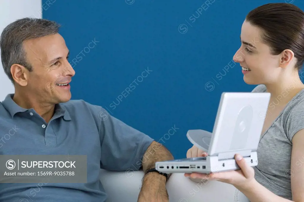 Teen girl showing her father portable DVD player, both smiling