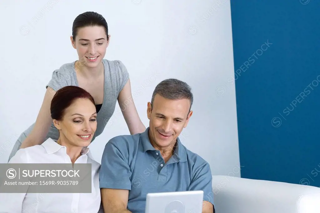 Family watching portable DVD player together, teen girl standing behind parents