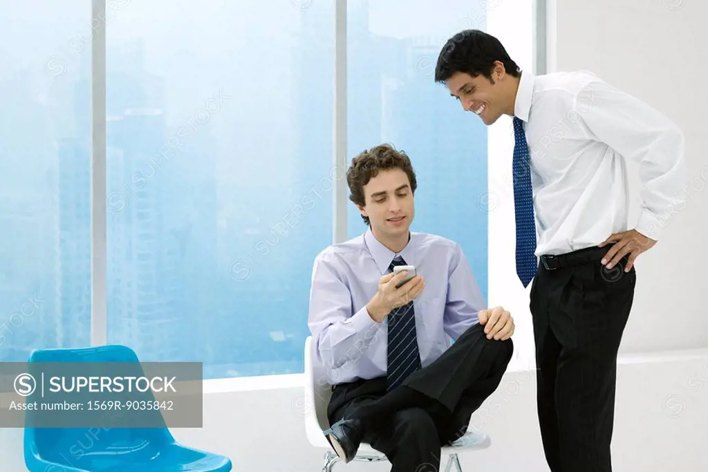 Young professional showing colleague his cell phone, both smiling