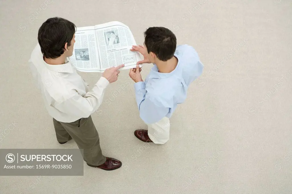 Two men looking at newspaper together, overhead view