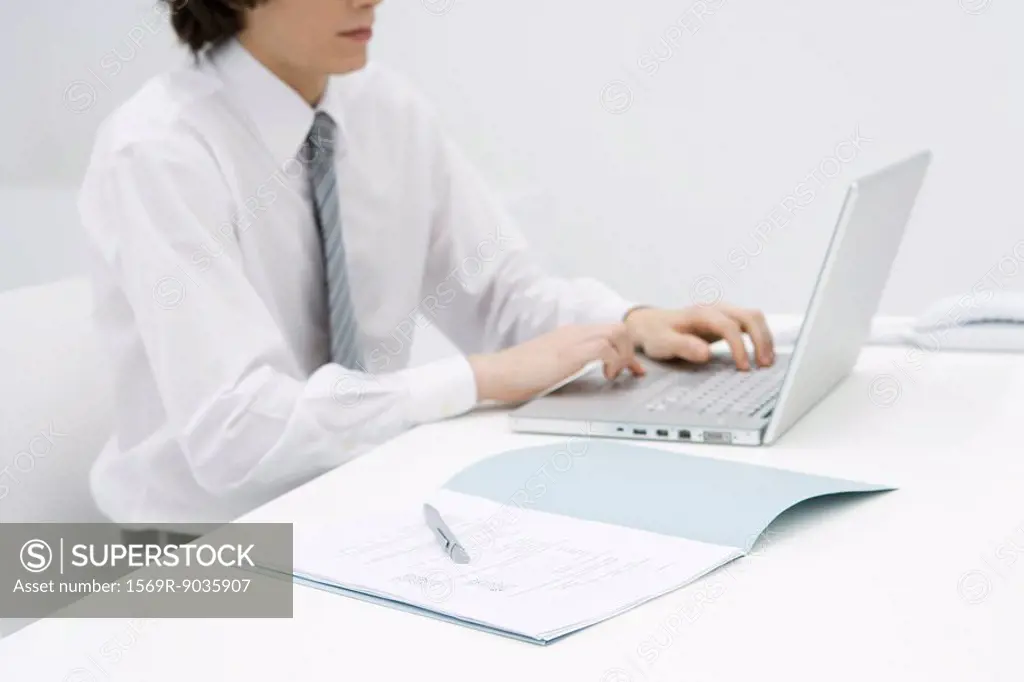 Male sitting at desk using laptop, cropped view